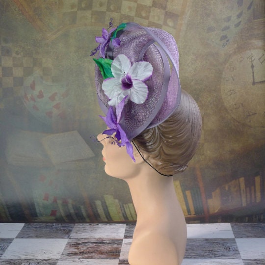 Amethyst Twist hat in shimmering lavendar sinamay headpiece with handmade orchids and hibiscus flowers, handsewn silk bias brim.  In Stock