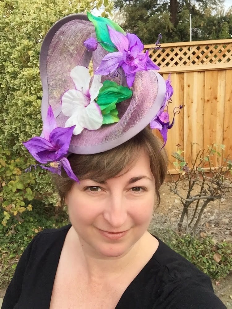 Amethyst Twist hat in shimmering lavendar sinamay headpiece with handmade orchids and hibiscus flowers, handsewn silk bias brim.  In Stock